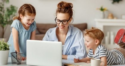 Eine Erzieherin verwendet ein Kita Verwaltungssoftware an einem Laptop und zwei Kinder schauen ihr dabei zu.