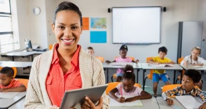 Eine Lehrerin verwendet eine Software für die Verwaltung ihrer Schülerinnen und Schüler auf einem Tablet vor ihrer Klasse.