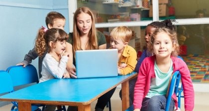 Eine Erzieherin sitzt mit Kindern in der Kita zusammen an einem Laptop.