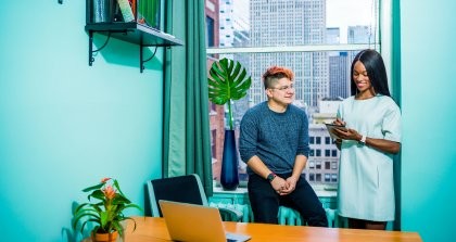 Zwei Menschen sitzen in einem Büro am Fenster und unterhalten sich