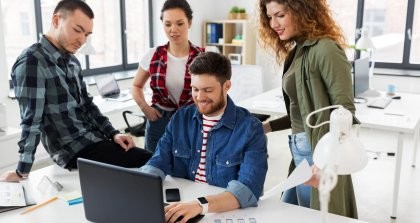 Ein junges Team sammelt sich um einen Laptop herum und arbeitet im Büro mit einer Bürosoftware