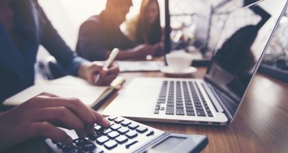 Eine Person erstellt online Rechnungen in einem Café an ihrem Laptop mit Taschenrechner.